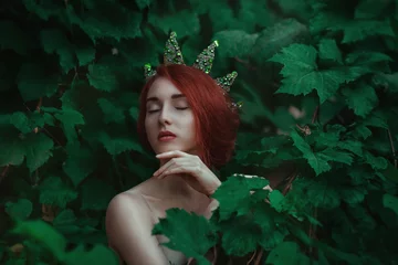 Fotobehang Portrait of a girl with red hair in a green leaves with a crown © oleg_ermak