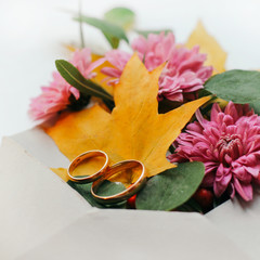Autumn bouquet of maple leaves and gold wedding ring in an envelope. Wedding card closeup. View from above.