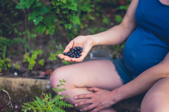 Pregnant woman with black currants in garden