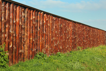 Long wooden fence made of oak tree trunks on green grass