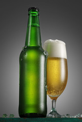 Bottle and glass of beer on the wooden table over grey background
