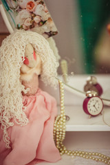 Pearl necklace surrounds pink doll standing before the mirror