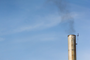 silver smoke stack with black smoke against blue sky 