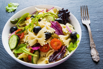 Pasta salad made from farfalle, red onion, cherry tomatoes, fresh cucumbers, black olives, mix of...