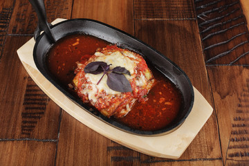 Baked zucchini and eggplant with tomato sauce in a pan. Wooden background.
