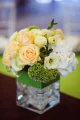 Beig roses and green flowers stand in a square green vase