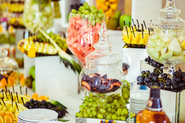 Cut fruits lie in glass bowls on the white buffet