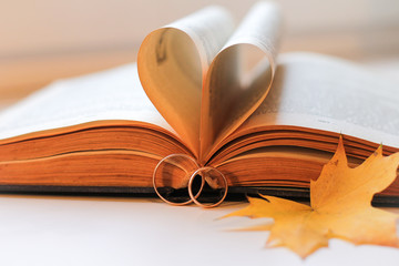 Open book with gold wedding rings and maple leaves. Wedding card with an autumn theme. - Powered by Adobe