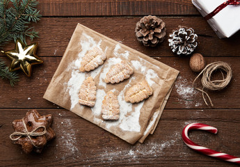 Sugar fir tree cookies on paper lying on wooden table with cones, branch, lavender and gift box. Christmas children meal concept.   