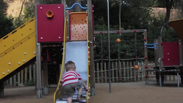 Young boy tries to climb up slide inside Park Guell located in Barcelona, Spain.