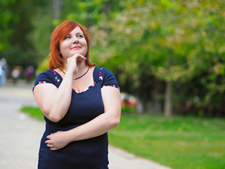 Portrait of attractive plus size redhead woman in a city park over blurred background