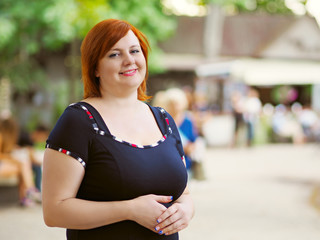 Portrait of attractive plus size redhead woman in a city park over blurred background