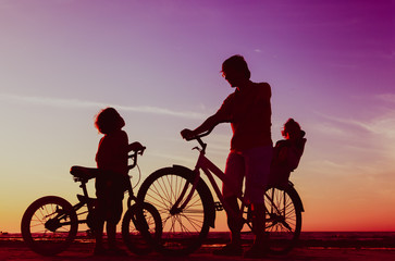 Obraz na płótnie Canvas Biker family silhouette, father with two kids on bikes at sunset