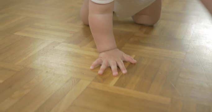 Close-up tracking shot of baby's hands and feet when crawling on wooden floor.
