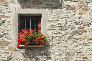 Fototapeta na wymiar Old window and red flowers in a stone house