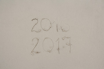 Message 2016 and 2017 written on sand at the beach. 2016 almost washed away by wave symbolizing...