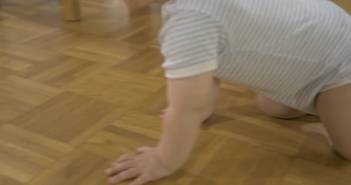 Side tracking shot of baby crawling at home on wooden floor.
