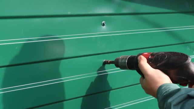 Fixing roofing screws, use a drill with a special nozzle. A worker attaches a roofing screw in a profiled metal sheet.Cladding of houses, buildings, fences , roofs using profiled sheets.