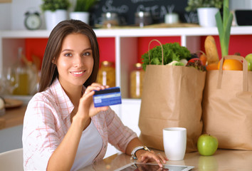 Smiling woman online shopping using tablet and credit card in kitchen