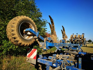 Martialisch anmutendes blaues Gerät für Landwirtschaft und Ackerbau mit schmutzigem Reifen auf dem Bauernhof bei blauem Himmel und Sonnenschein in Asemissen bei Bielefeld in Ostwestfalen-Lippe