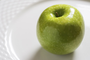 Green Apple on the White Plate. Shiny Organic Granny Smith Close Up.