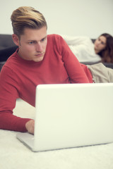 blond man looking at laptop and woman lying on couch