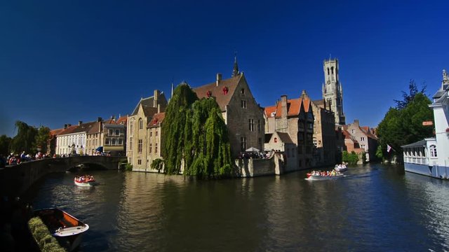 City scape of the canals of Bruges on a sunny day with Belfry in the background.