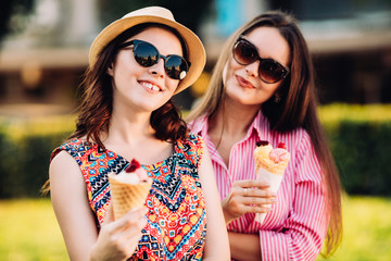 Portrait of two young women standing together eating ice cream. Happy young female friends outdoor.
