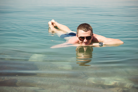 Man in sunglasses relaxing on water surface Dead Sea. Tourism recreation, healthy lifestyle concept. Peaceful smile
