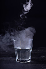 Hot water with a lot of steam in a glass at a black background. Dark photo