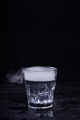 Hot water with a lot of steam in a glass at a black background. Dark photo. Concept photo: three state of water - ice, water, steam.