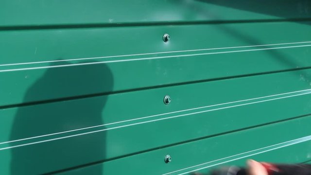 Fixing roofing screws, use a drill with a special nozzle. A worker attaches a roofing screw in a profiled metal sheet.Cladding of houses, buildings, fences , roofs using profiled sheets.