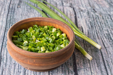  Green onions.   Green onions, sliced in a wooden bowl and whole feathers, on an old wooden table.
