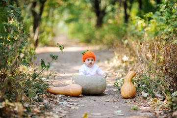 baby girl in the orange cap in the form of a pumpkin sitting inside a huge pumpkin on a background autumn forest. Celebrating Halloween
