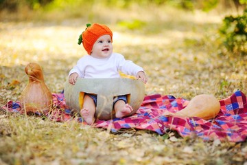 baby girl in the orange cap in the form of a pumpkin sitting inside a huge pumpkin on a background autumn forest. Celebrating Halloween