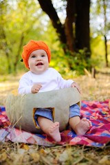 baby girl in the orange cap in the form of a pumpkin sitting inside a huge pumpkin on a background autumn forest. Celebrating Halloween
