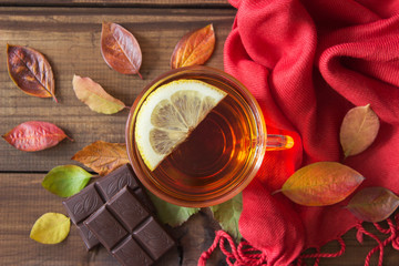 Cup of tea with slice of lemon and chocolate with autumn leaves on old wooden table.