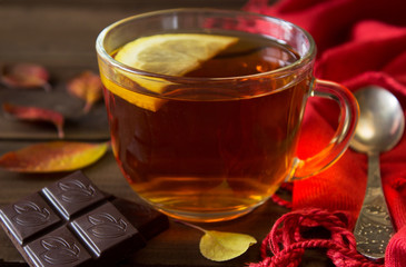 Cup of tea with slice of lemon and chocolate with autumn leaves on old wooden table.
