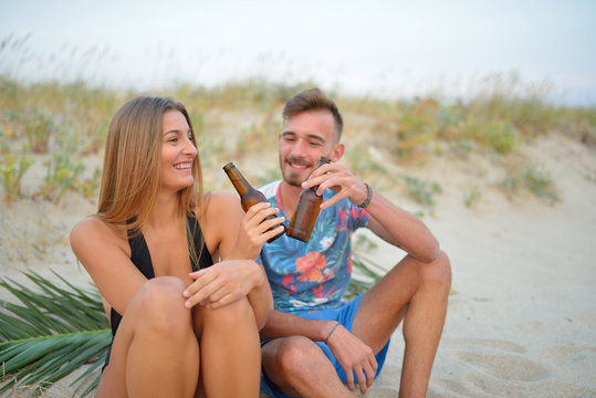 Lovely couple drinking beer sitting on beach.