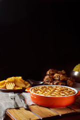 Wooden table served for Thanksgiving dinner. Close view at pumpkin pie. Chips, chicken legs, and mash potatoes on a black background. Vertical shot. Dark photo