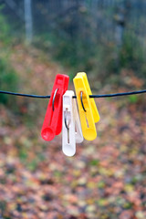 Three colored clothepins hanging on black rope on a blurred background in autumn day outdoors closeup