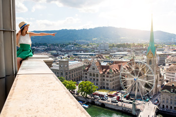 Top view on Zurich city with young woman showing sitting on the tower's top. Woman having a great...