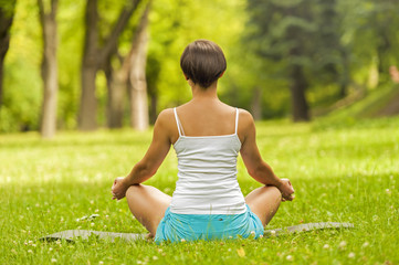 Naklejka na ściany i meble Woman meditating and doing yoga in park back.