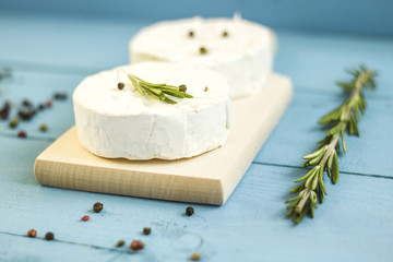 Round camembert cheese mold with rosemary on wooden board