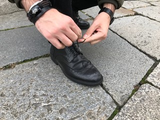 Man tying shoelaces in the street, black shoes