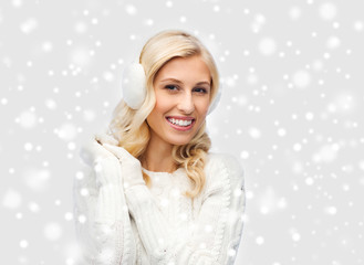 smiling young woman in winter earmuffs and sweater