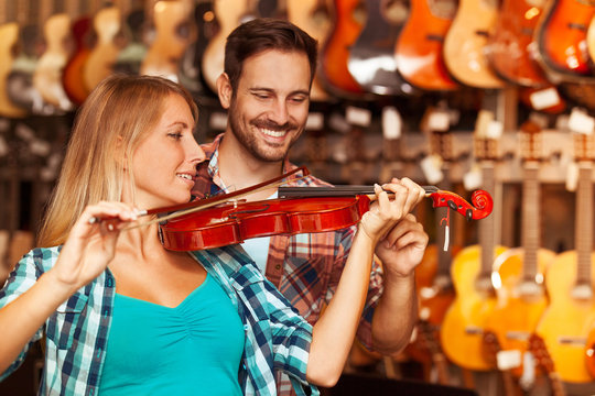 Young woman is playing violin in musical instruments store.