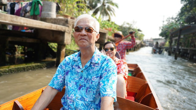 Asian Chinese elderly couple having fun retirment trip around the world, cruising in floating market, Thailand