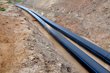 The process of laying of engineering and heating systems. Two black plastic pipes are in a trench...