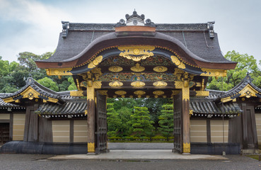 Kyoto, Japan - September 19, 2016: Majestic Kara-mon gate at the Nijo Castle. Plenty of gold trimmings and colorful woodwork. Cloudy sky and green foliage in background.